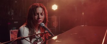 Movie still from “A Star Is Born” (2018), directed by Bradley Cooper – A woman with long red hair sitting at a piano; Close Up shot, Low angle