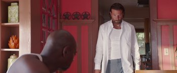 Movie still from “A Star Is Born” (2018), directed by Bradley Cooper – A man standing in front of another man in front of a red wall; Medium shot, Over the shoulder angle