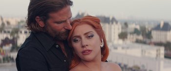 Movie still from “A Star Is Born” (2018), directed by Bradley Cooper – A man kissing a woman's face in front of some buildings; Close Up shot, Over the shoulder angle