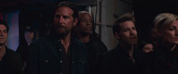 Movie still from “A Star Is Born” (2018), directed by Bradley Cooper – A group of men standing next to each other in a room; Medium shot, Over the shoulder angle