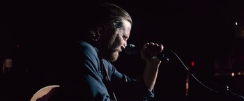 Movie still from “A Star Is Born” (2018), directed by Bradley Cooper – A man with long hair is singing into a microphone; Close Up shot, Low angle