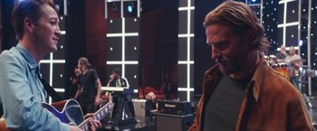 Movie still from “A Star Is Born” (2018), directed by Bradley Cooper – A man playing a guitar in front of a group of people; Medium shot, Over the shoulder angle