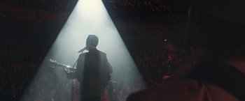 Movie still from “A Star Is Born” (2018), directed by Bradley Cooper – A man standing in front of a microphone on a stage; Wide shot, Over the shoulder angle