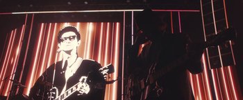 Movie still from “A Star Is Born” (2018), directed by Bradley Cooper – A man holding a guitar in front of a picture of a man; Close Up shot, Low angle