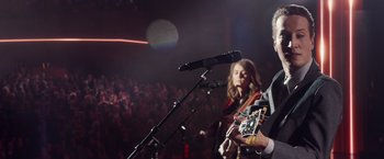 Movie still from “A Star Is Born” (2018), directed by Bradley Cooper – A man and a woman are playing guitar in front of an audience; Medium shot, Over the shoulder angle