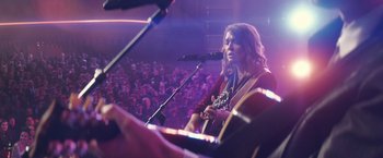 Movie still from “A Star Is Born” (2018), directed by Bradley Cooper – A woman playing a guitar in front of an audience; Medium shot, Over the shoulder angle
