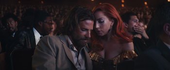 Movie still from “A Star Is Born” (2018), directed by Bradley Cooper – A man and a woman sitting next to each other in a crowd; Close Up shot, Low angle
