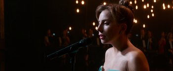 Movie still from “A Star Is Born” (2018), directed by Bradley Cooper – A beautiful young woman holding a microphone in front of a crowd of onlookers; Close Up shot, Over the shoulder angle
