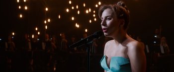 Movie still from “A Star Is Born” (2018), directed by Bradley Cooper – A woman in a blue dress singing into a microphone in front of a crowd of onlookers; Close Up shot, Over the shoulder angle