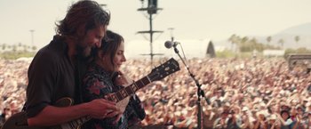 Movie still from “A Star Is Born” (2018), directed by Bradley Cooper – A man and a woman playing a guitar in front of an audience; Medium shot, Over the shoulder angle