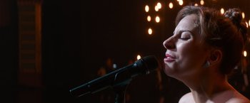 Movie still from “A Star Is Born” (2018), directed by Bradley Cooper – A woman is speaking into a microphone in front of lights; Close Up shot, Low angle