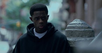 A man in a black hoodie is standing next to a stone wall