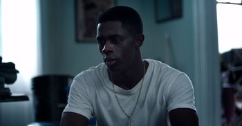 A young man wearing a white t - shirt is sitting at a table