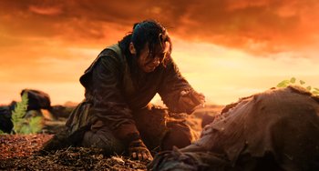 Movie still from “A Writer's Odyssey” (2021), directed by Yang Lu – A man kneeling down next to a dead body in a field; Medium shot, Low angle