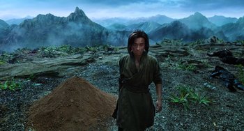 Movie still from “A Writer's Odyssey” (2021), directed by Yang Lu – A man standing in the middle of a field with mountains in the background; Medium shot, High angle