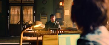 Movie still from “A Writer's Odyssey” (2021), directed by Yang Lu – A man sitting at a table in front of a computer monitor; Medium shot, Over the shoulder angle