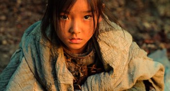 Movie still from “A Writer's Odyssey” (2021), directed by Yang Lu – A young girl is sitting on the ground looking at the camera; Close Up shot, High angle