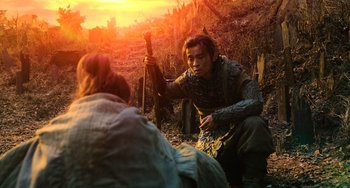 Movie still from “A Writer's Odyssey” (2021), directed by Yang Lu – A man holding a stick in a field at sunset; Medium shot, Over the shoulder angle