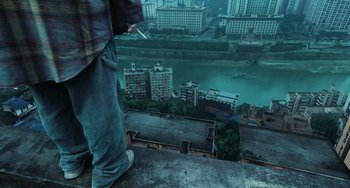 Movie still from “A Writer's Odyssey” (2021), directed by Yang Lu – A man standing on the edge of a building looking down at a river; Wide shot, High angle