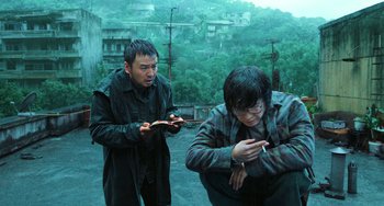 Movie still from “A Writer's Odyssey” (2021), directed by Yang Lu – Two men looking at their cell phones on the roof of a building; Medium shot, High angle