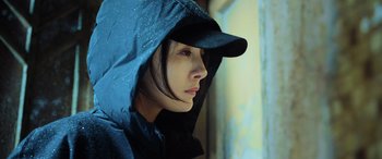 Movie still from “A Writer's Odyssey” (2021), directed by Yang Lu – A woman wearing a rain coat and a hat; Close Up shot, Low angle