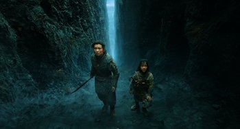 Movie still from “A Writer's Odyssey” (2021), directed by Yang Lu – A man and a child are standing in a cave; Wide shot, High angle