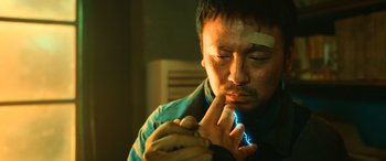 Movie still from “A Writer's Odyssey” (2021), directed by Yang Lu – A man with a bandage on his face looking at a piece of paper; Close Up shot, Low angle