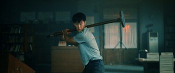 Movie still from “A Writer's Odyssey” (2021), directed by Yang Lu – A man holding a baseball bat in a room; Medium shot, Low angle