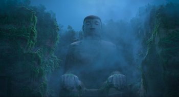 Movie still from “Abominable” (2019), directed by Todd Wilderman – A large statue of a person sitting in the middle of a forest; Extreme Wide shot, Low angle