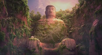 Movie still from “Abominable” (2019), directed by Todd Wilderman – A large buddha statue sitting in the middle of a lush green forest; Extreme Wide shot, Low angle