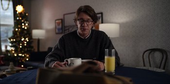 Movie still from “About Fate” (2022), directed by Marius Vaysberg – A man sitting at a table with a glass of orange juice; Medium shot, Over the shoulder angle