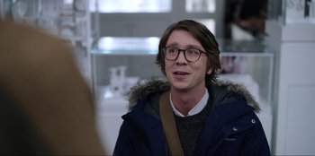 Movie still from “About Fate” (2022), directed by Marius Vaysberg – A young man wearing glasses and a blue jacket; Medium shot, Over the shoulder angle