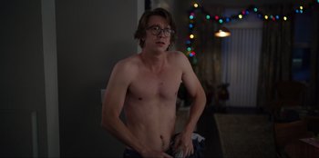 Movie still from “About Fate” (2022), directed by Marius Vaysberg – A man with glasses is standing in front of a christmas tree; Medium shot, Over the shoulder angle