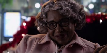 Movie still from “About Fate” (2022), directed by Marius Vaysberg – An older woman wearing glasses and a pink coat; Close Up shot, Over the shoulder angle