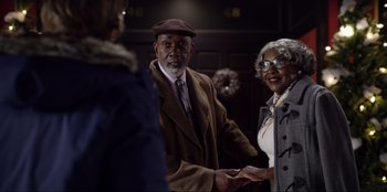 Movie still from “About Fate” (2022), directed by Marius Vaysberg – An older man and woman holding hands in front of another man; Medium shot, Over the shoulder angle