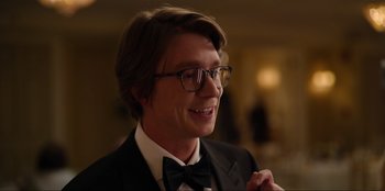 Movie still from “About Fate” (2022), directed by Marius Vaysberg – A man in a suit and bow tie smiling for the camera; Close Up shot, Over the shoulder angle