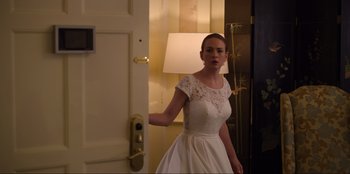 Movie still from “About Fate” (2022), directed by Marius Vaysberg – A woman in a white dress standing in front of a door; Medium shot, Over the shoulder angle