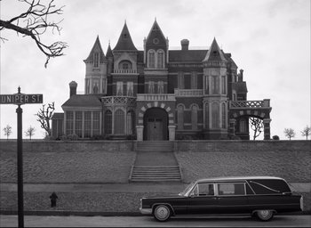 Movie still from “The French Dispatch” (2021), directed by Wes Anderson – A black and white photo of a hearse parked in front of an old mansion; Extreme Wide shot, Low angle