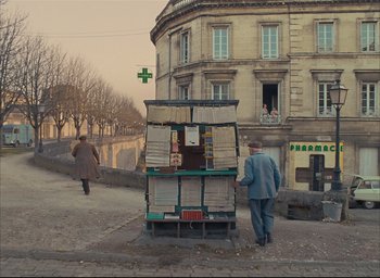 Movie still from “The French Dispatch” (2021), directed by Wes Anderson – A man walking down the street next to a newspaper stand; Extreme Wide shot, High angle