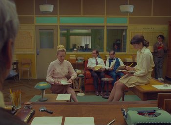 Movie still from “The French Dispatch” (2021), directed by Wes Anderson – A group of people sitting in a room with papers; Wide shot, High angle