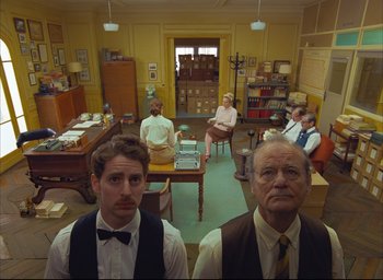 Movie still from “The French Dispatch” (2021), directed by Wes Anderson – A group of people sitting in a room; Wide shot, Low angle