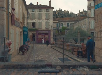 Movie still from “The French Dispatch” (2021), directed by Wes Anderson – People are walking down a street in a small town; Extreme Wide shot, High angle