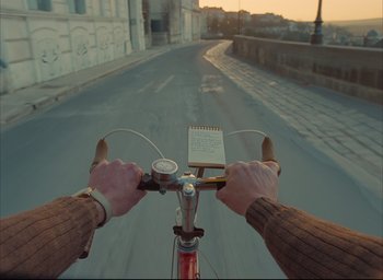 Movie still from “The French Dispatch” (2021), directed by Wes Anderson – A person riding a bike down a street; Close Up shot, Overhead angle