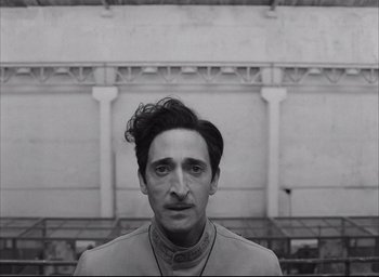 Movie still from “The French Dispatch” (2021), directed by Wes Anderson – A black and white photo of a man with a mustache; Close Up shot, Low angle