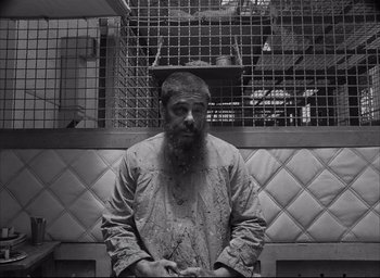 Movie still from “The French Dispatch” (2021), directed by Wes Anderson – A man with a long beard sitting on a bench; Medium shot, Overhead angle