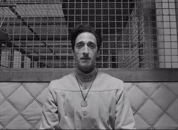 Movie still from “The French Dispatch” (2021), directed by Wes Anderson – A black and white photo of a man wearing a necklace; Close Up shot, Low angle