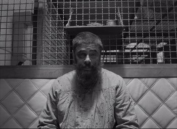 Movie still from “The French Dispatch” (2021), directed by Wes Anderson – Black and white photograph of a man with a beard; Medium shot, Overhead angle