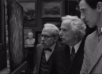 Movie still from “The French Dispatch” (2021), directed by Wes Anderson – A group of men standing next to each other in a room; Medium shot, Over the shoulder angle