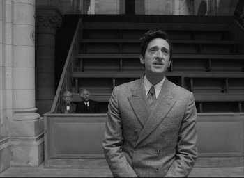 Movie still from “The French Dispatch” (2021), directed by Wes Anderson – A black and white photo of a man in a suit and tie; Medium shot, Low angle