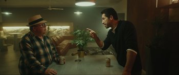 Movie still from “Accident Man: Hitman's Holiday” (2022), directed by George Kirby – Two people sitting at a table talking to each other; Medium shot, Over the shoulder angle